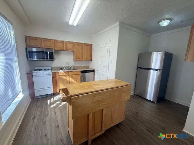 a kitchen with stainless steel appliances granite countertop a refrigerator a stove a sink dishwasher and a microwave with wooden floor