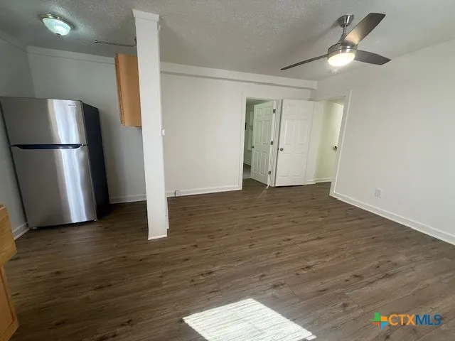 a view of an empty room with wooden floor and a ceiling fan