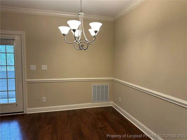 an empty room with wooden floor chandelier and windows