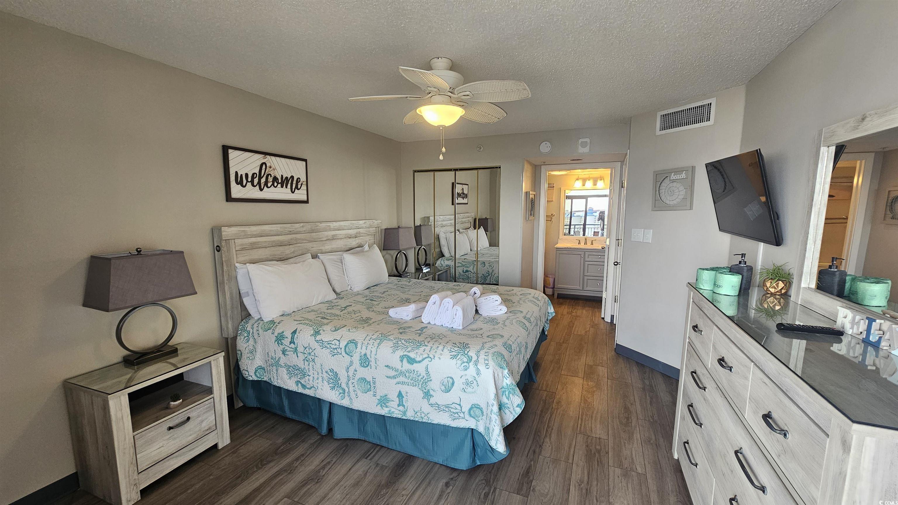 201 74th Avenue North, Unit 1201 Myrtle Beach, SC 29572 - Photo 3 of 40 Bedroom featuring a closet, a textured ceiling, dark wood finished floors, a ceiling fan, and ensuite bath