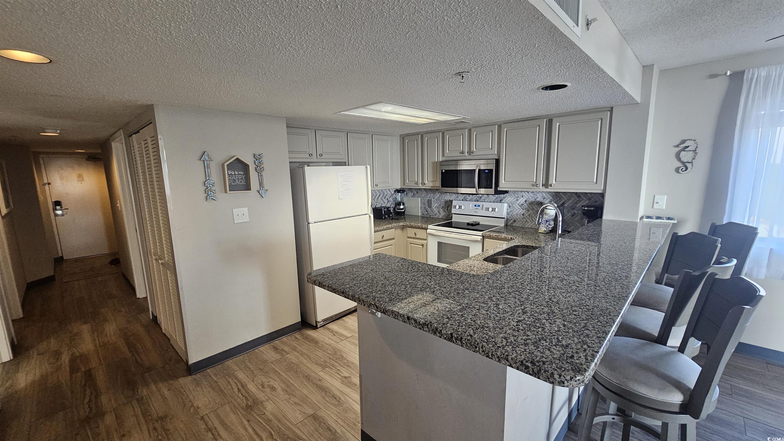 201 74th Avenue North, Unit 1201 Myrtle Beach, SC 29572 - Photo 6 of 40 Kitchen with white appliances, a peninsula, a textured ceiling, a kitchen bar, and dark wood-style flooring