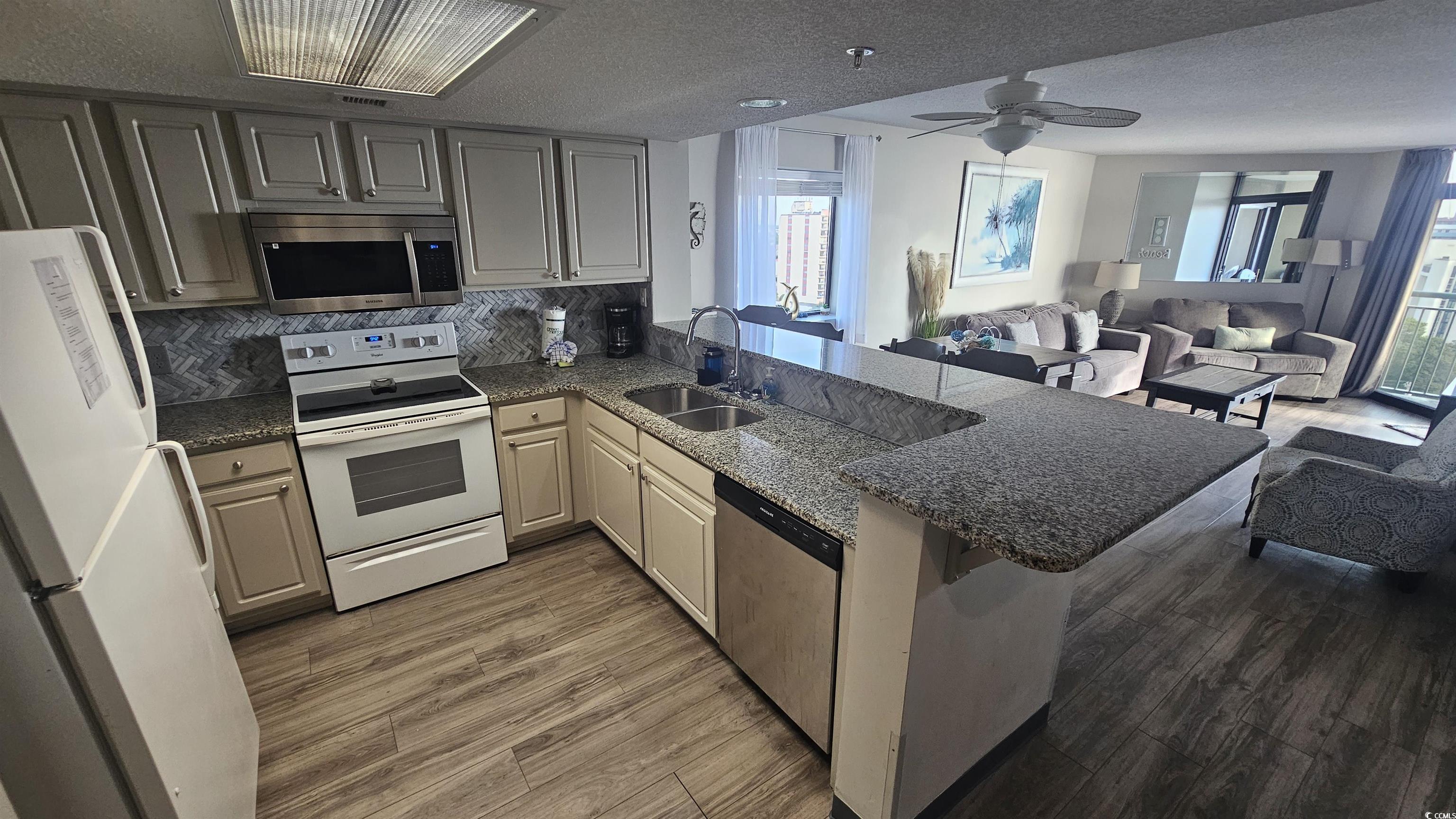 201 74th Avenue North, Unit 1201 Myrtle Beach, SC 29572 - Photo 9 of 40 Kitchen with a peninsula, stainless steel appliances, dark stone countertops, dark wood-style flooring, and a textured ceiling