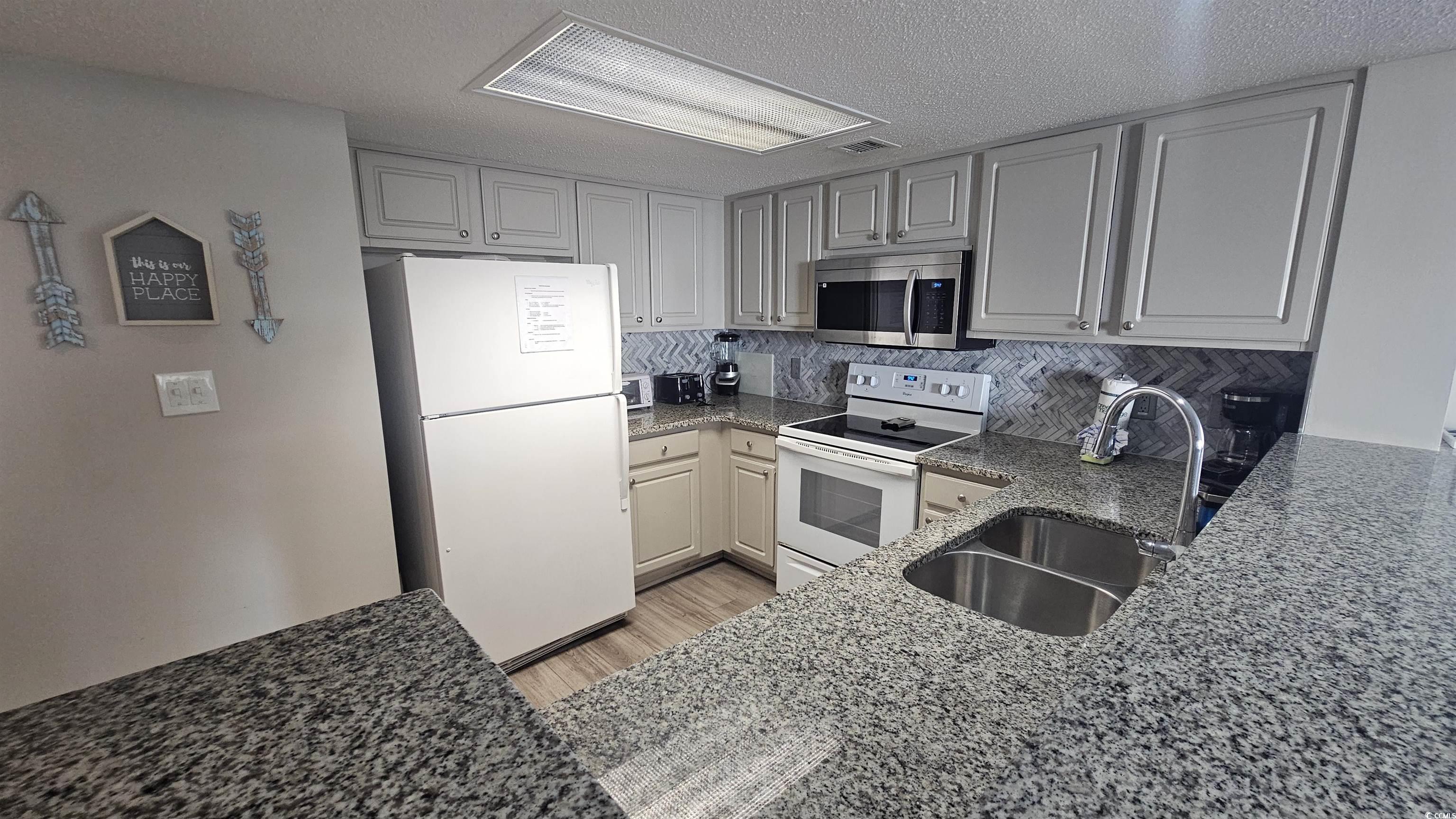 201 74th Avenue North, Unit 1201 Myrtle Beach, SC 29572 - Photo 10 of 40 Kitchen featuring dark stone counters, white appliances, light wood-style flooring, tasteful backsplash, and a textured ceiling