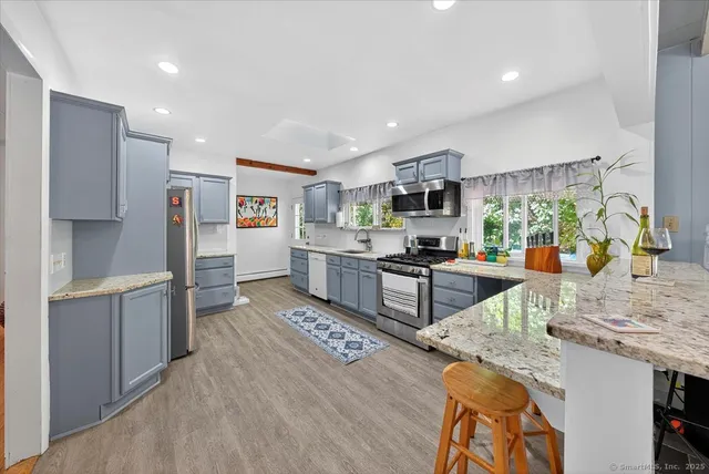 a kitchen with stainless steel appliances granite countertop a stove top oven a sink a refrigerator and white cabinets with wooden floor