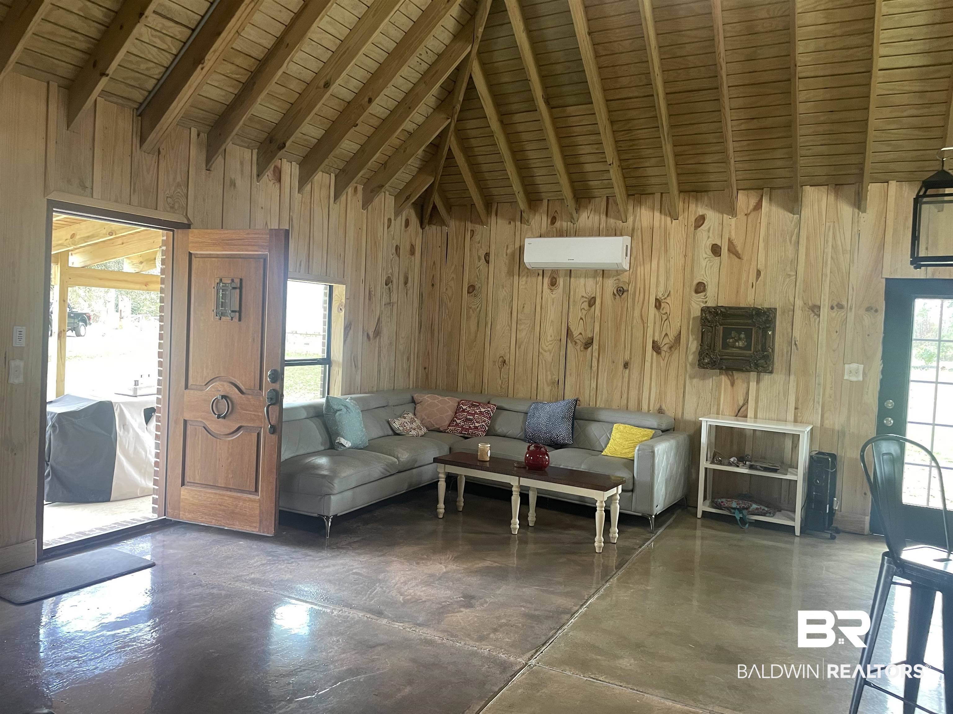 21593 Hubbard Road Robertsdale, AL 36567 - Photo 19 of 22 Living area featuring lofted ceiling with beams, wooden walls, concrete flooring, and a wall unit AC