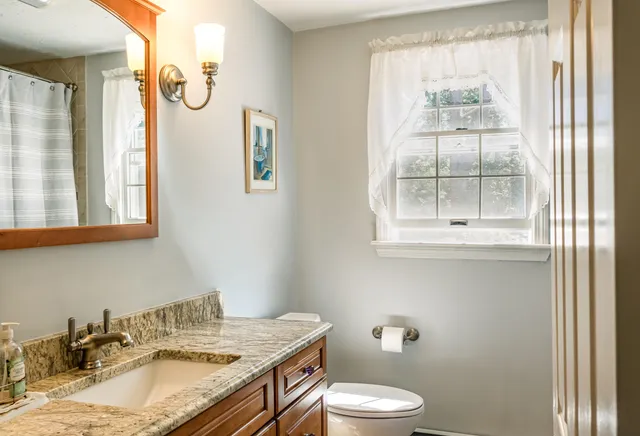 a bathroom with a granite countertop sink toilet and a window