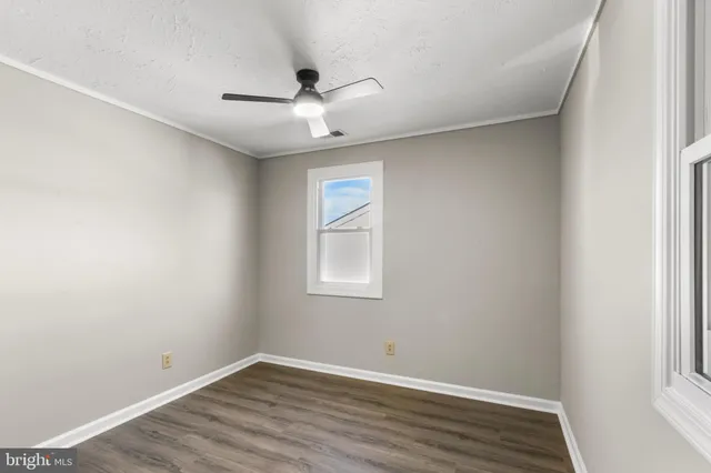 an empty room with wooden floor ceiling fan and windows