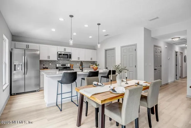 a kitchen with stainless steel appliances kitchen island granite countertop a dining table chairs refrigerator and sink