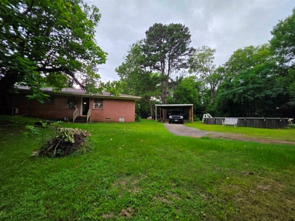 4514 West Loop 281 Longview, TX 75604 - Photo 8 of 36 Brick exterior with a large green lawn, wood-frame carport, and an above-ground pool