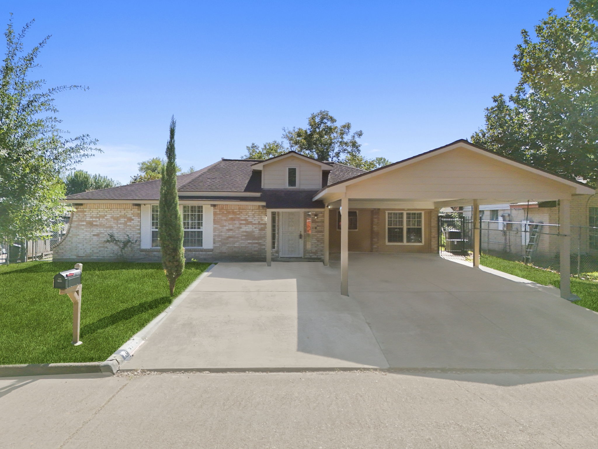 This photo shows a single-story brick home with a neatly manicured lawn. It features a large carport and a welcoming front porch. The driveway is spacious, and the property has mature trees, offering a cozy suburban feel.