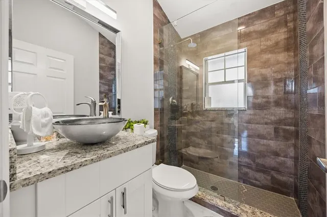 a bathroom with a granite countertop sink a toilet a mirror and shower