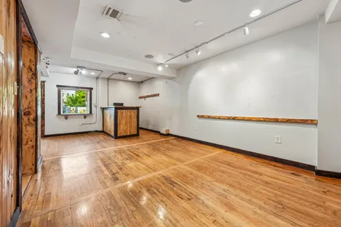 an empty room with wooden floor and way to kitchen