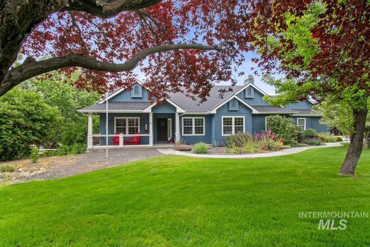 Blue exterior with white trim, featuring a covered front porch, dormer windows, and a manicured lawn
