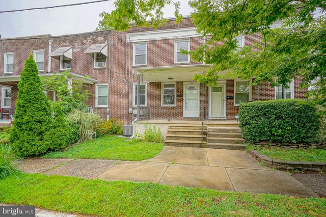 a view of a brick house with many windows plants and large trees