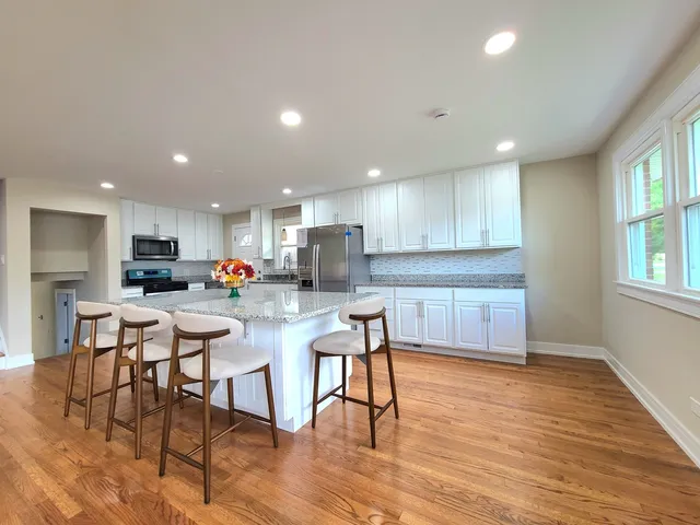a kitchen with stainless steel appliances kitchen island granite countertop a stove a sink a refrigerator and a dining table with wooden floor