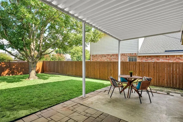 a view of a patio with table and chairs under an umbrella with a small yard