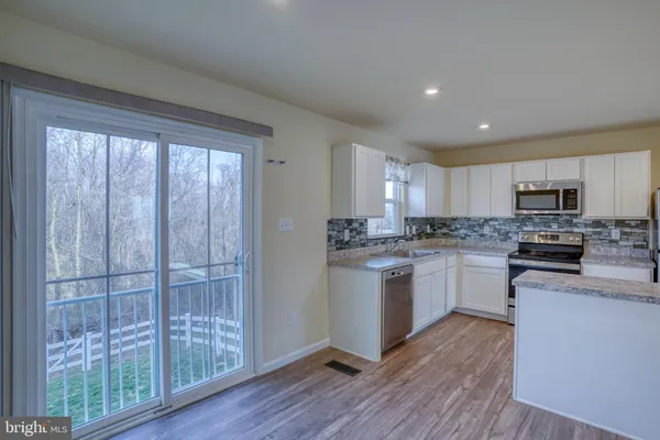 a kitchen with stainless steel appliances granite countertop a refrigerator a sink a stove top oven and wooden floors