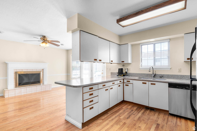1822 East 9800th Street South Sandy, UT 84092 - Photo 31 of 38 Kitchen with light wood-style floors, white cabinets, a peninsula, and a tiled fireplace
