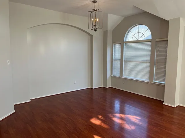 an empty room with wooden floor a chandelier fan and windows