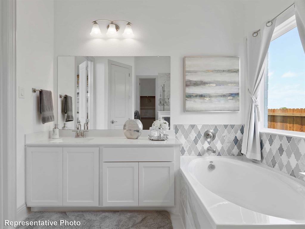 2204 Ridgecrest Lane Anna, TX 75409 - Photo 10 of 17 White bathroom featuring a built-in tub with decorative tile surround, a single vanity with a quartz-style countertop, and a large mirror with overhead light fixture