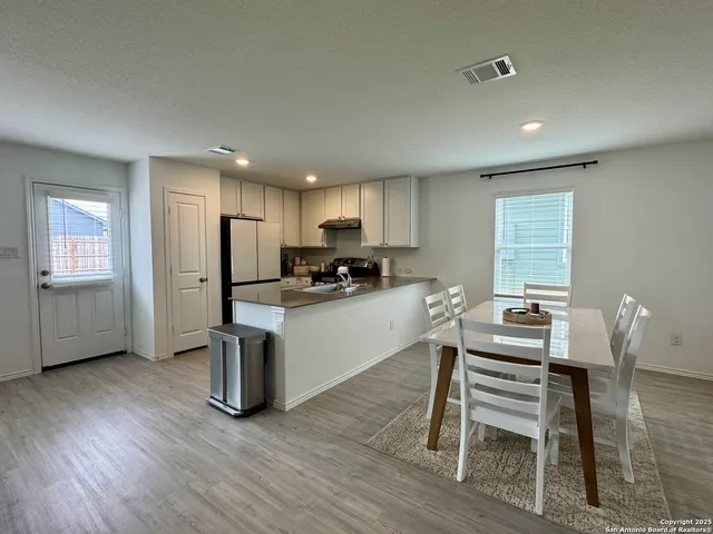 a kitchen with stainless steel appliances granite countertop a stove a sink a refrigerator dining table and chairs with wooden floor