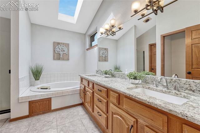 2690 Spaatz Road Monument, CO 80132 - Photo 18 of 50 Bathroom featuring tiled tub, dual vanity, tile patterned flooring, vaulted ceiling with skylight, and a notable chandelier