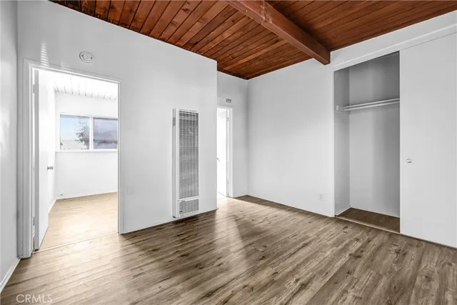 a view of an empty room with wooden floor and a kitchen