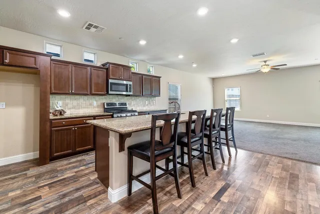 a kitchen with stainless steel appliances kitchen island granite countertop a stove a refrigerator a oven a sink with a dining table and chairs
