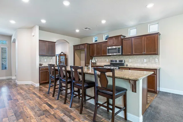 a open kitchen with stainless steel appliances granite countertop a stove top oven a sink dishwasher a dining table and chairs with wooden floor