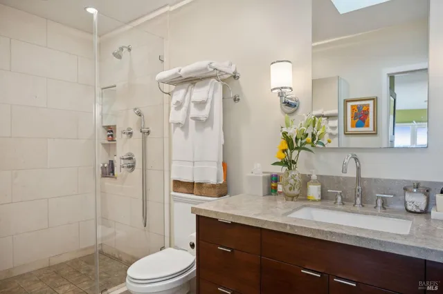 a bathroom with a granite countertop sink a toilet a mirror a vanity and shower