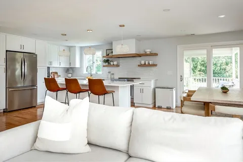 a living room with stainless steel appliances kitchen island granite countertop a table chairs and a refrigerator