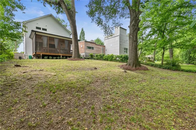 a view of a yard in front of a white house with plants and large tree
