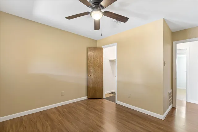 an empty room with wooden floor chandelier fan and closet area with wooden floor