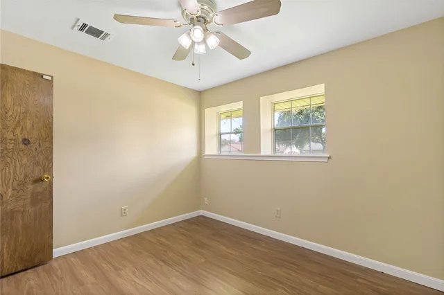 an empty room with wooden floor chandelier fan and windows