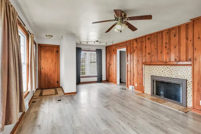 a view of a livingroom with wooden floor a fireplace a ceiling fan and windows
