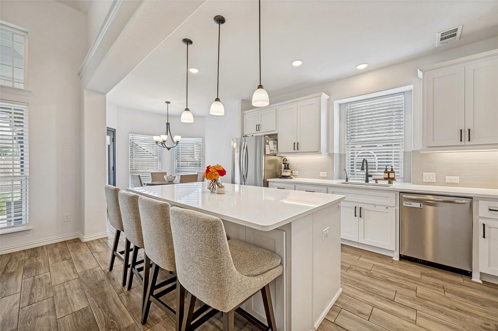 808 Violet Way Celina, TX 75009 - Photo 8 of 30 Kitchen featuring white cabinetry, wood finish floors, stainless steel appliances, a breakfast bar area, and tasteful backsplash.