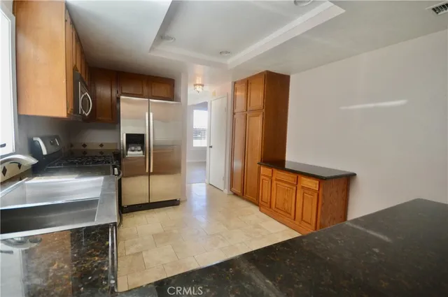 a kitchen with stainless steel appliances granite countertop a refrigerator a stove and a sink with wooden cabinets