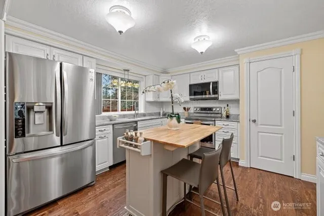 a kitchen with stainless steel appliances a refrigerator a stove a sink dishwasher a dining table and chairs with wooden floor