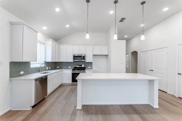 a large white kitchen with stainless steel appliances granite countertop a stove a sink a refrigerator and white cabinets with wooden floor