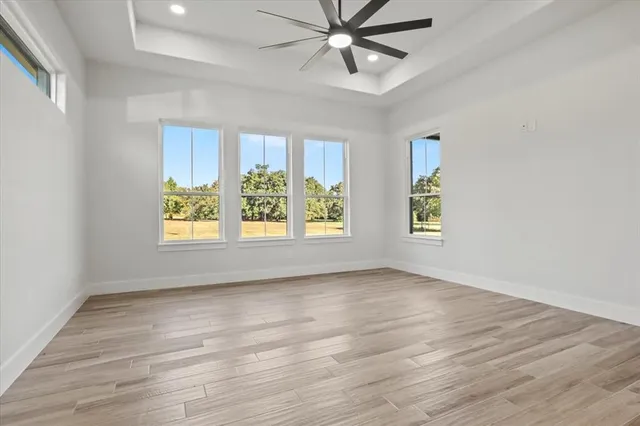 an empty room with wooden floor chandelier fan and windows