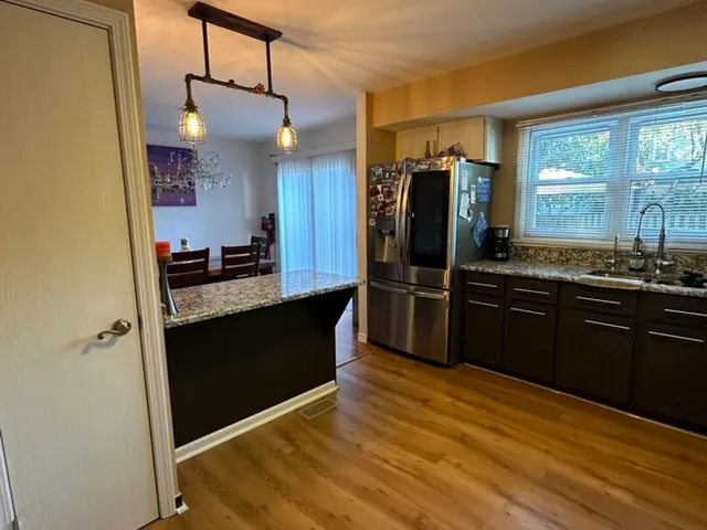 a kitchen with stainless steel appliances kitchen island granite countertop a refrigerator a sink dishwasher a stove and white countertops with wooden floor