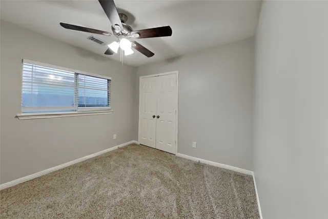 an empty room with a chandelier fan and windows