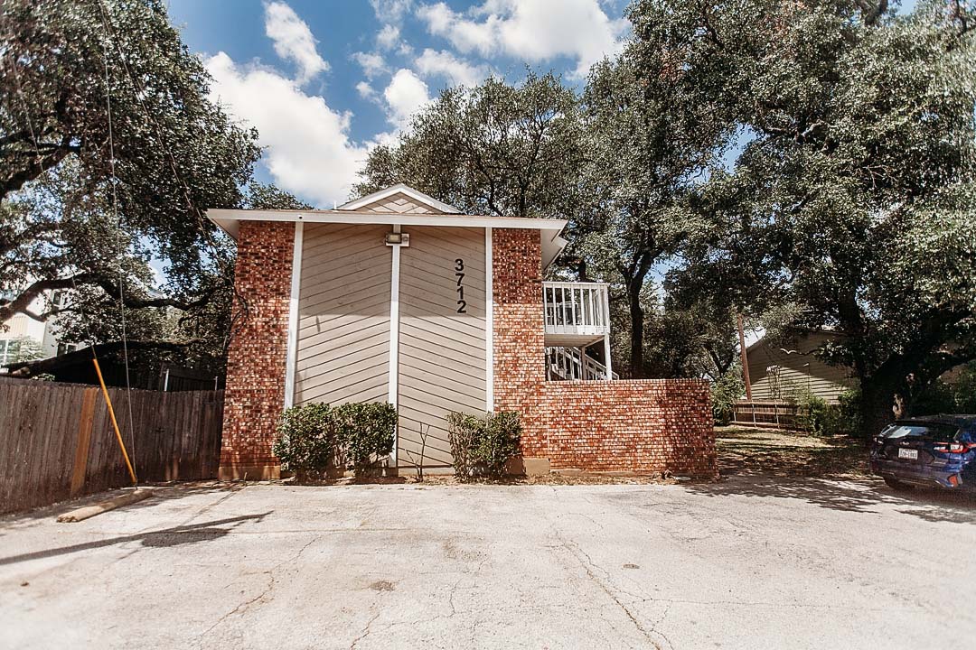 3712 Menchaca Road, Unit 7 Austin, TX 78704 - Photo 1 of 13 Mature trees shade a classic brick and wood exterior featuring a private upper balcony.