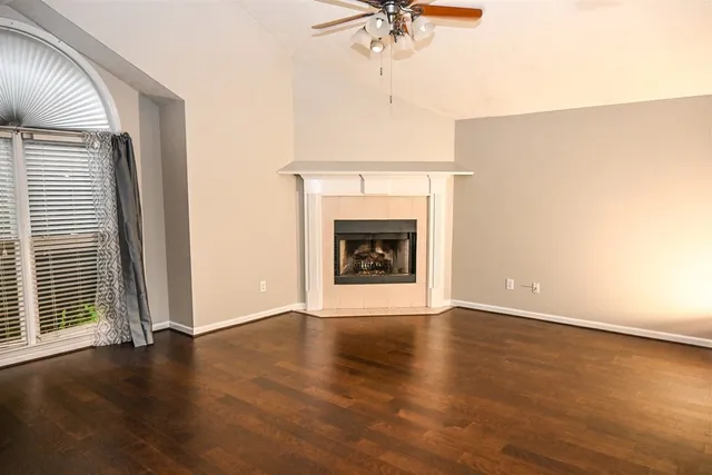 an empty room with wooden floor fireplace and windows
