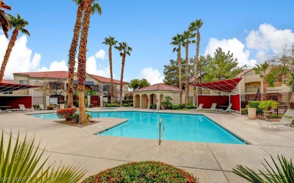 7885 West Flamingo Road, Unit 1008 Las Vegas, NV 89147 - Photo 2 of 29 Relax poolside in this inviting outdoor oasis, featuring palm trees and a vibrant red canopy.