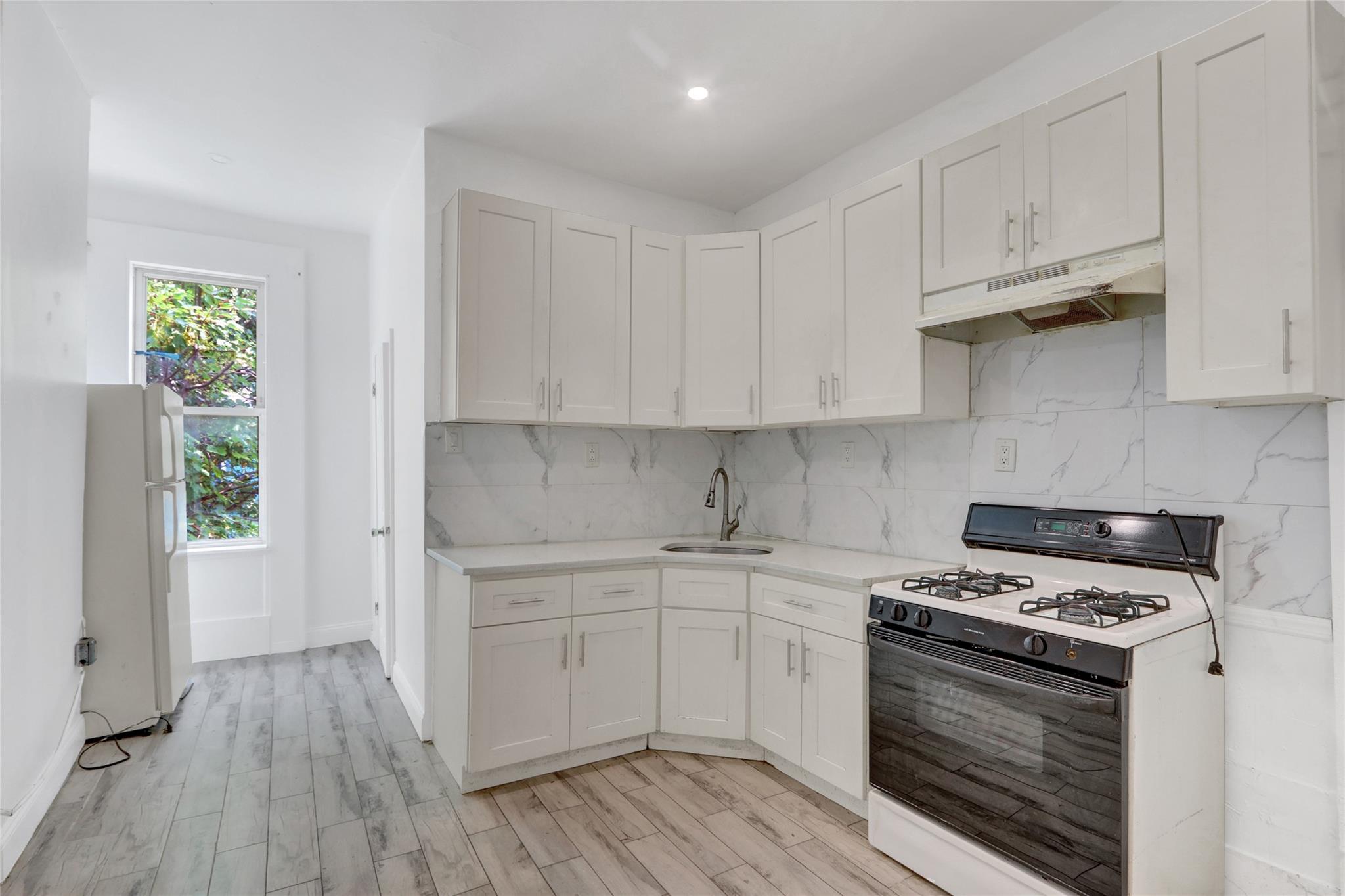 119-15 101st Avenue Queens, NY 11419 - Photo 3 of 20 Kitchen featuring white appliances, under cabinet range hood, decorative backsplash, light wood-type flooring, and white cabinetry