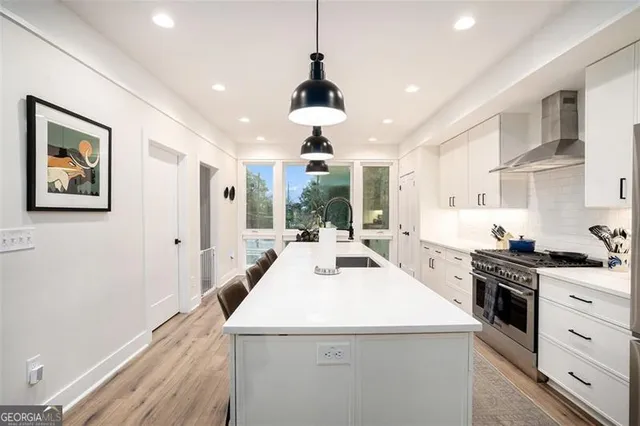 a kitchen with stainless steel appliances a stove a sink dishwasher a refrigerator white cabinets and wooden floor next to a window