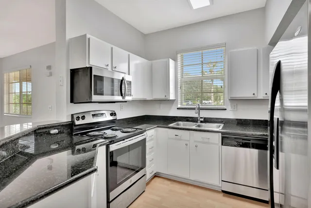 a kitchen with granite countertop a sink cabinets stainless steel appliances and a window