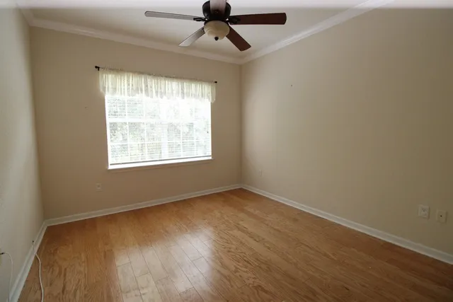 an empty room with wooden floor ceiling fan and windows