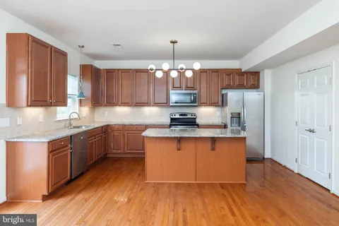 a kitchen with stainless steel appliances granite countertop wooden cabinets a refrigerator a sink a stove a microwave and wooden floors